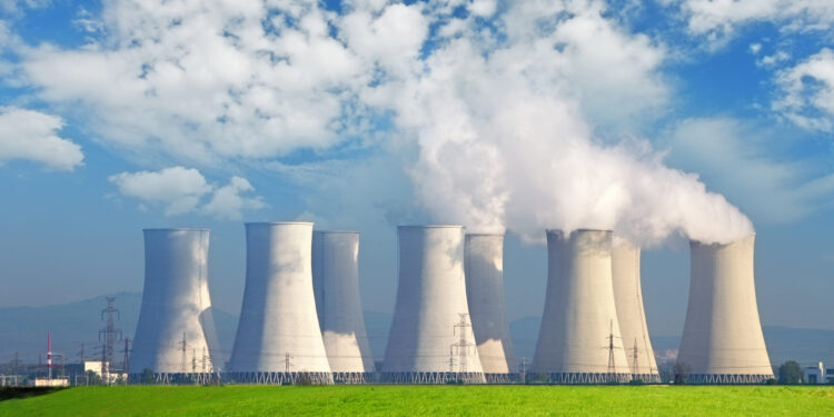 Central nuclear con campo verde y grandes nubes azules